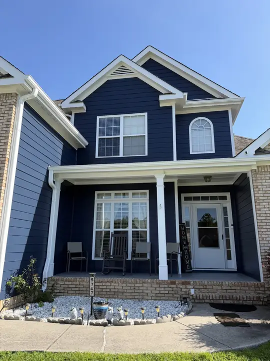 Two-story home with deep navy lap siding, white trim and covered front porch after exterior painting in Ooltewah, TN