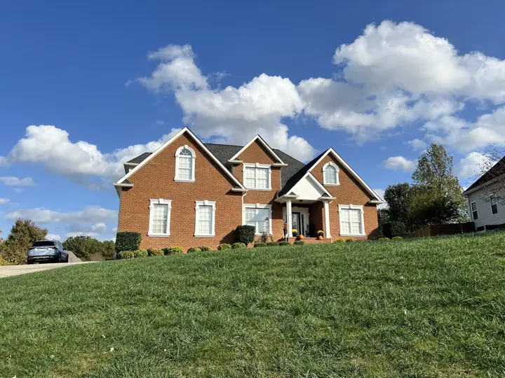 Red brick home on a hill with white trim under a blue sky in Ooltewah, TN