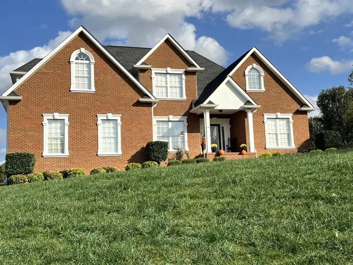 Red brick home with bright white window surrounds, gables and portico after trim painting in Ooltewah, TN