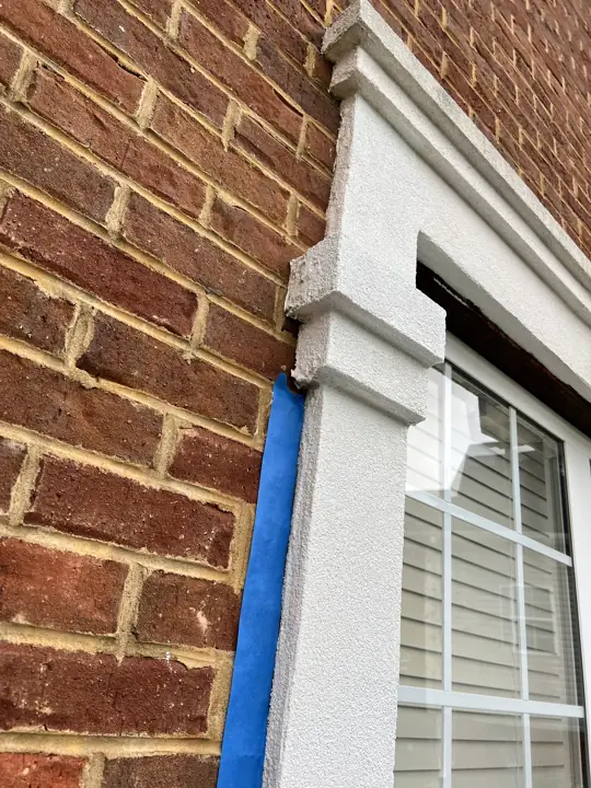 Blue tape masking brick beside a window surround before painting in Ooltewah, TN