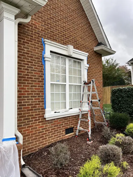 Window surround masked with tape and a ladder set for trim painting in Ooltewah, TN