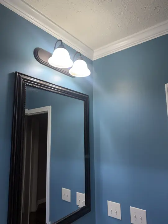 Blue bathroom wall with dark framed mirror, vanity light and white crown molding in Cleveland, TN