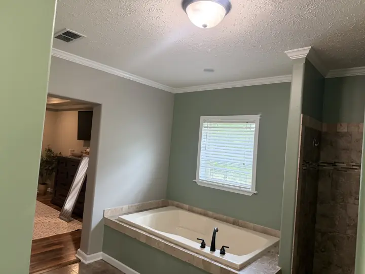 Sage green primary bathroom with soaking tub, white window trim and crown molding in Cleveland, TN
