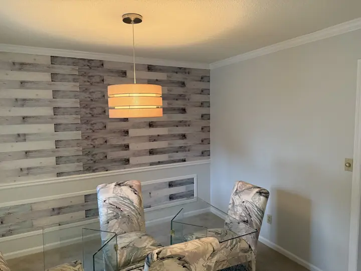 Dining room with pale gray walls, white chair rail and plank accent wall above glass table in Harrison, TN