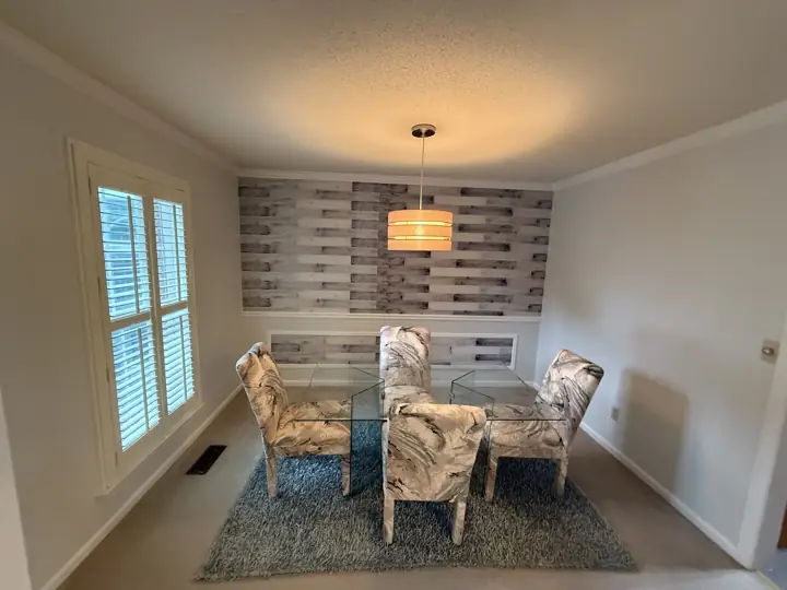Pale gray dining room with white crown molding, plantation shutters and wood plank accent wall in Harrison, TN