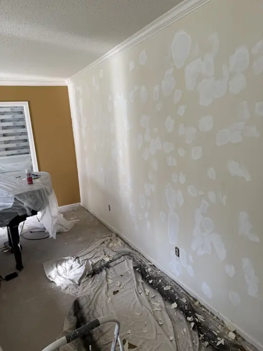 Living room wall with many patched holes, piano wrapped in plastic and drop cloths during prep in Harrison, TN