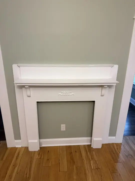 Front view of white painted fireplace mantel with carved detail on sage green wall, Chattanooga, TN