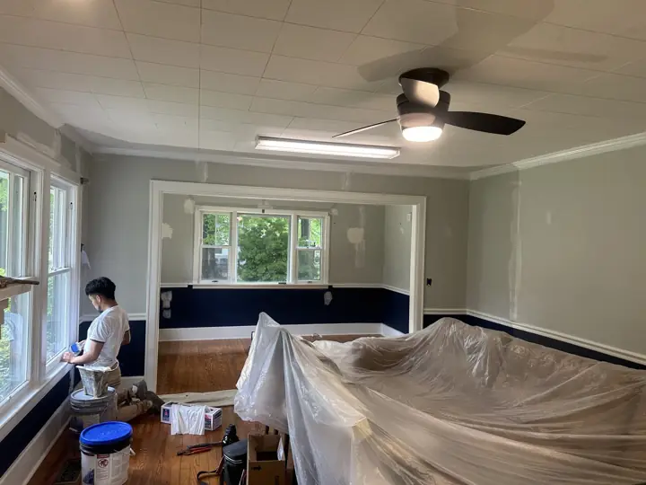 Painter cutting in near the windows with furniture wrapped in plastic during interior painting in Ringgold, GA