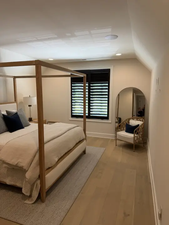 Bedroom under a sloped ceiling with warm white walls and black window shutters in Chattanooga, TN
