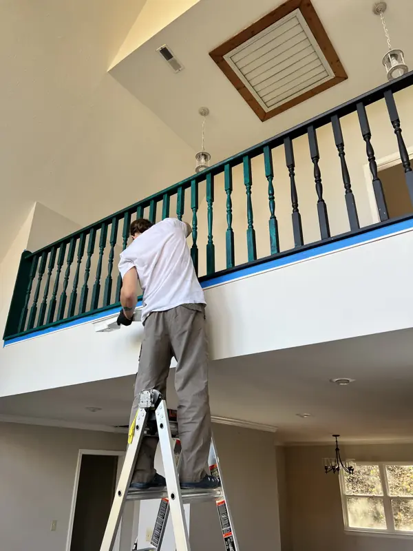 Painter on a ladder finishing a loft balcony railing in Trenton, GA