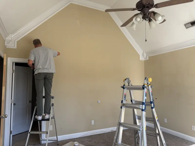 Painter on a ladder painting a vaulted bedroom wall in Chattanooga, TN