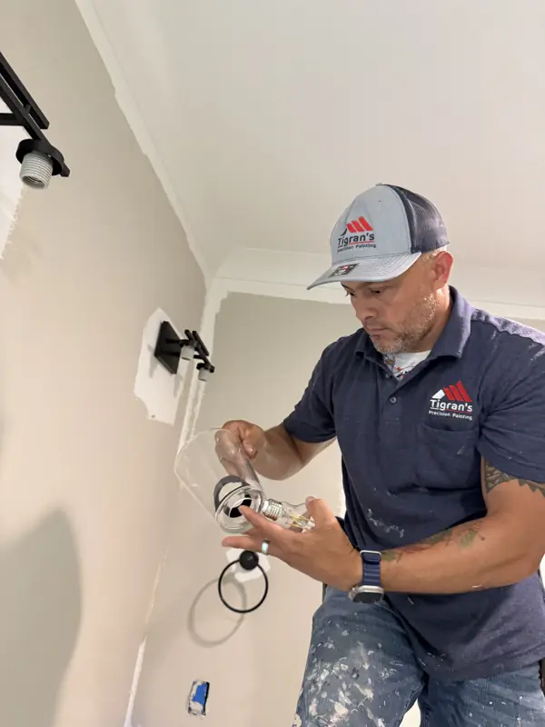 Crew member in a company cap and shirt reinstalling a light fixture after paint in Soddy-Daisy, TN