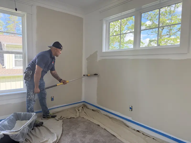 Painter rolling a bedroom wall, floor covered and baseboards taped in Soddy-Daisy, TN